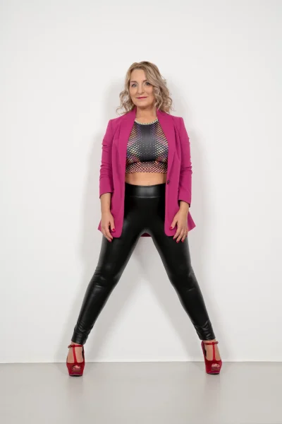 Corinna Anders, eine Schlagersängerin, trägt schwarze Lederhosen und einen rosa Blazer.